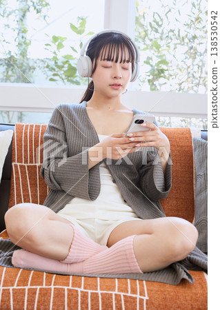 A woman using her smartphone with headphones: A lifestyle enjoyed at home A woman using her smartphone with headphones: A lifestyle enjoyed at home 138530542