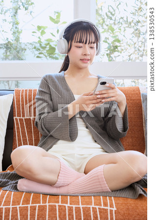 A woman using her smartphone with headphones: A lifestyle enjoyed at home A woman using her smartphone with headphones: A lifestyle enjoyed at home 138530543