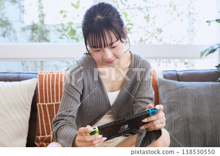 A woman playing a handheld game console; relaxing at home on a holiday. 138530550