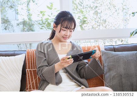 一位女士正在玩掌上游戲機;她在假期裡待在家裡放鬆。 一位女士正在玩掌上游戲機;她在假期裡待在家裡放鬆。 138530552