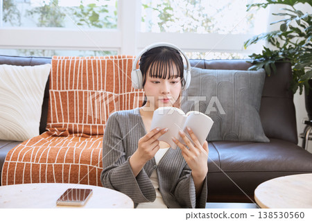 一位女士戴著耳機聽音樂，在家放鬆看書。 138530560