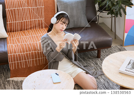 一位女士戴著耳機聽音樂,在家放鬆看書。 一位女士戴著耳機聽音樂,在家放鬆看書。 138530563