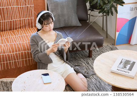 A woman reading a book while listening to music on headphones – relaxing at home. A woman reading a book while listening to music on headphones – relaxing at home. 138530564