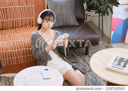 一位女士戴著耳機聽音樂,在家放鬆看書。 一位女士戴著耳機聽音樂,在家放鬆看書。 138530565