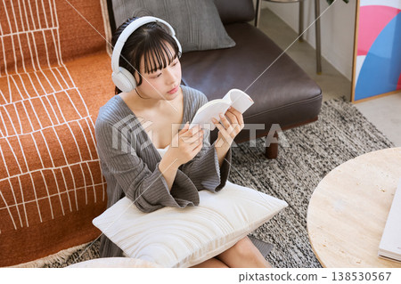 A young woman thinking while reading a book with headphones on. A young woman thinking while reading a book with headphones on. 138530567
