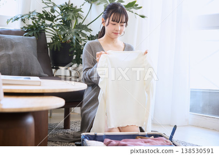 一位年輕女子正在把衣服裝進行李箱,準備旅行。 一位年輕女子正在把衣服裝進行李箱,準備旅行。 138530591