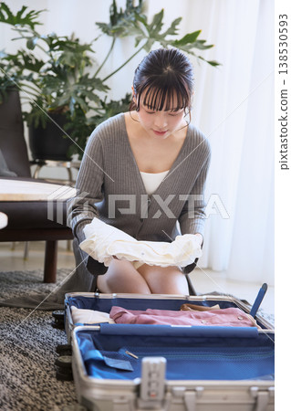 一位年輕女子正在把衣服裝進行李箱，準備旅行。 138530593