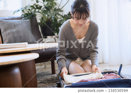 一位年輕女子正在把衣服裝進行李箱，準備旅行。 138530594
