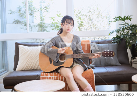 A young woman playing an acoustic guitar in her living room at home. A young woman playing an acoustic guitar in her living room at home. 138530600