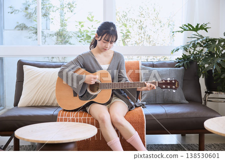 A young woman playing an acoustic guitar in her living room at home. A young woman playing an acoustic guitar in her living room at home. 138530601