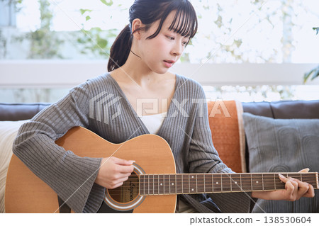 一位年輕女子在家彈奏原聲吉他 一位年輕女子在家彈奏原聲吉他 138530604
