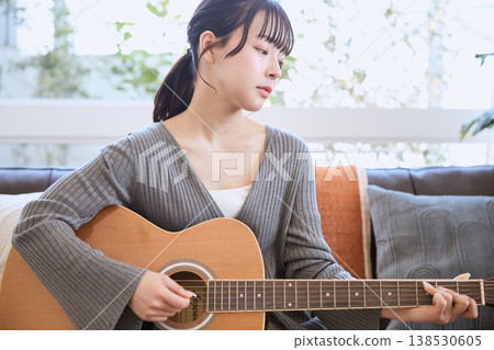 一位年輕女子在家彈奏原聲吉他 138530605