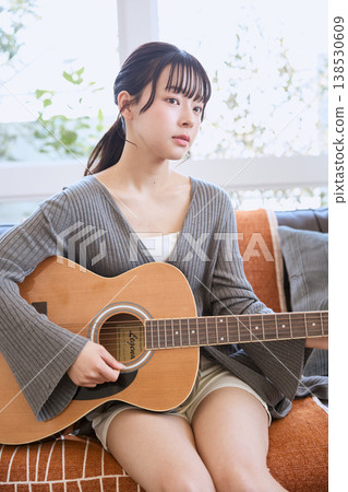 一位年輕女子在家彈奏原聲吉他 一位年輕女子在家彈奏原聲吉他 138530609