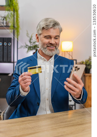Middle-aged businessman confirms payment on smartphone holding credit card smiling at smooth service Middle-aged businessman confirms payment on smartphone holding credit card smiling at smooth service 138530610