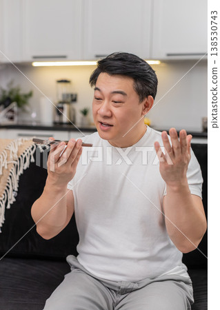 Asian man on phone loudspeaker explains decision with hand gestures ends call with warm goodbye sign 138530743