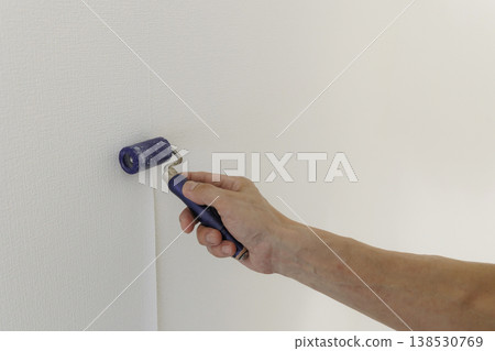 A hand repairing wallpaper seams with a roller. Image of wallpaper replacement during renovation or DIY. 138530769