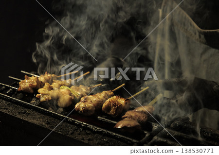 Yakitori grilled over charcoal, with smoke rising intensely – a scene of skilled craftsmanship in a traditional Japanese pub. 138530771