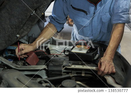 A mechanic's hands and tester during a car inspection and maintenance: measuring battery voltage and performing engine compartment maintenance. 138530777