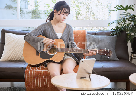 A young woman playing an acoustic guitar while looking at a tablet. A young woman playing an acoustic guitar while looking at a tablet. 138530797