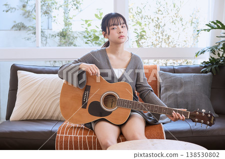 A young woman holding an acoustic guitar in her living room at home. A young woman holding an acoustic guitar in her living room at home. 138530802