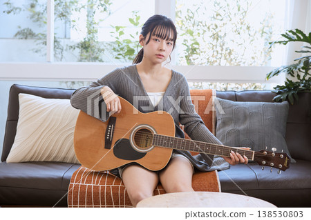 一位年輕女子在家中客廳抱著一把木吉他。 138530803