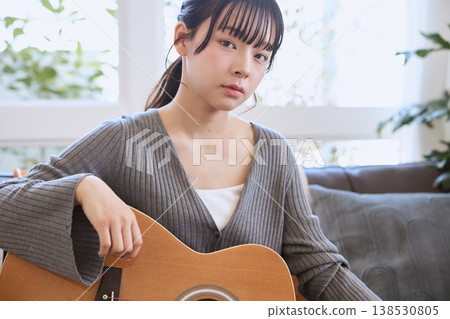 一位年輕女子在家中客廳抱著一把木吉他。 一位年輕女子在家中客廳抱著一把木吉他。 138530805