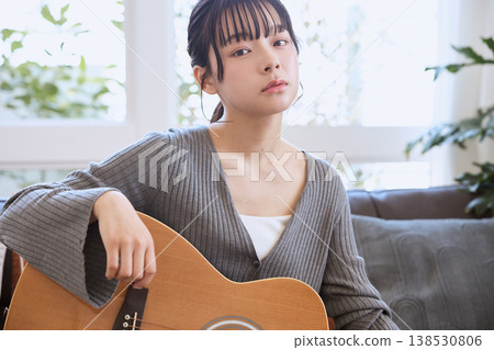 一位年輕女子在家中客廳抱著一把木吉他。 138530806