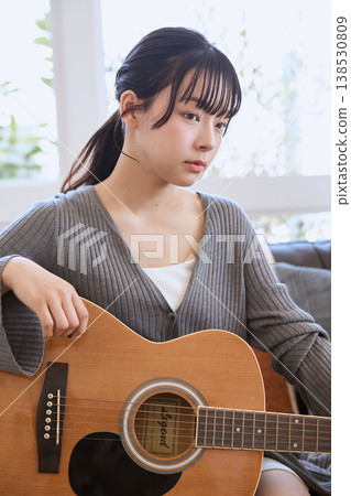 一位年輕女子在家中客廳抱著一把木吉他。 一位年輕女子在家中客廳抱著一把木吉他。 138530809