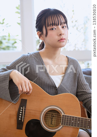 一位年輕女子在家中客廳抱著一把木吉他。 一位年輕女子在家中客廳抱著一把木吉他。 138530810