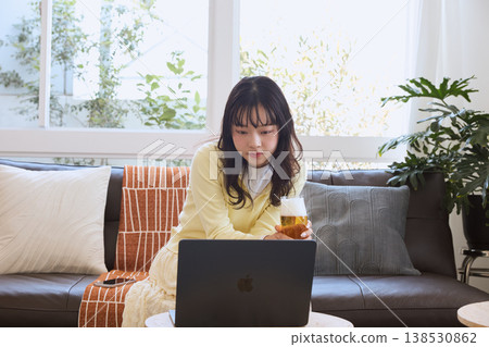 一位女士在家一邊喝啤酒一邊看影片。 一位女士在家一邊喝啤酒一邊看影片。 138530862
