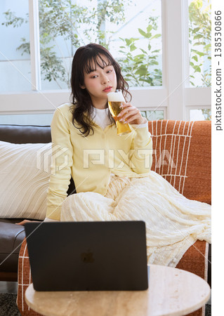 一位女士在家一邊喝啤酒一邊看影片。 一位女士在家一邊喝啤酒一邊看影片。 138530866