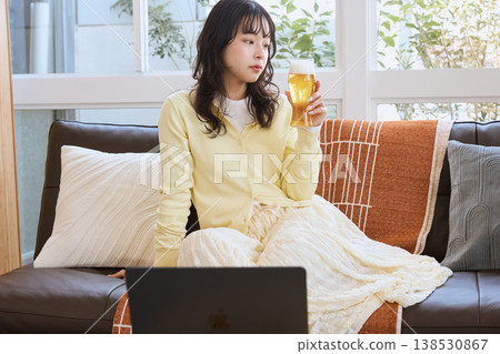一位女士在家一邊喝啤酒一邊看影片。 138530867