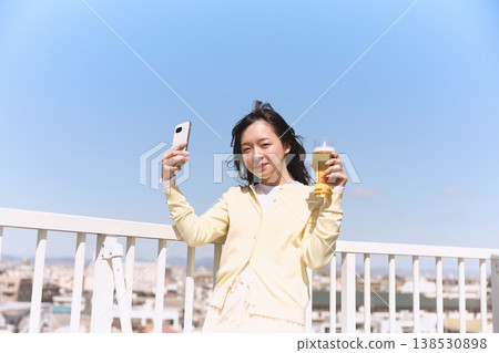 一位女士在戶外一邊喝飲料一邊拿著智慧型手機；在藍天下自拍，這是一種生活方式。 138530898