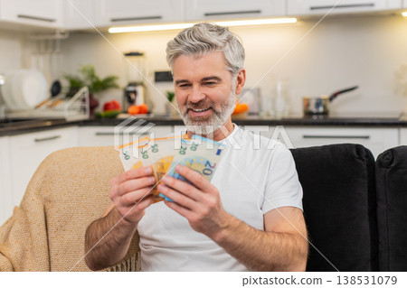 Middle-aged man counts money cash euros smiles at big plans purchase salary bonus savings investment 138531079