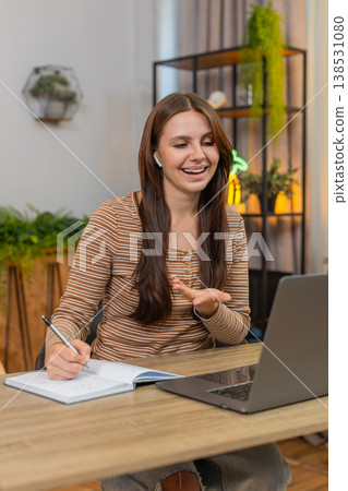 Young woman in headphones on video call gestures and writes notes in notebook while focused on work Young woman in headphones on video call gestures and writes notes in notebook while focused on work 138531080