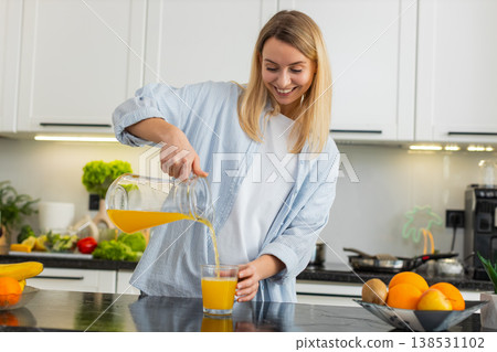 Young woman pouring fresh orange juice into glass for healthy fit breakfast vitamins in home kitchen 138531102