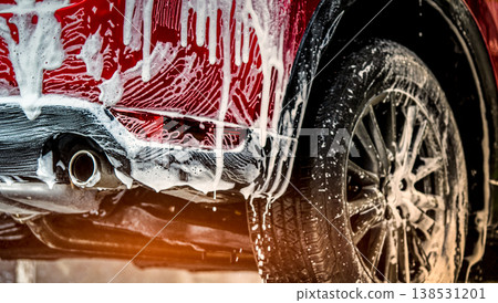Red compact SUV car with sport and modern design washing with soap. Car covered with white foam. Car care service business concept. Car wash with foam before glass waxing and glass coating automobile. 138531201