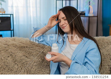 Woman suffering severe headache sitting holding head exhausted searching taking pain relief pills Woman suffering severe headache sitting holding head exhausted searching taking pain relief pills 138531254