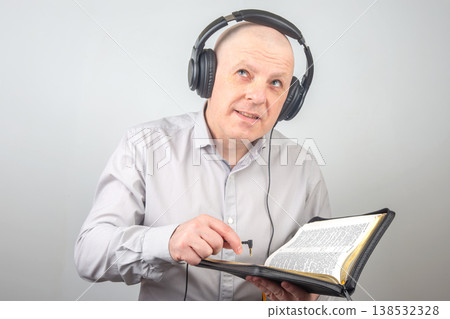 Man listens to audio while reading the Bible in a quiet space on a weekday morning Man listens to audio while reading the Bible in a quiet space on a weekday morning 138532328