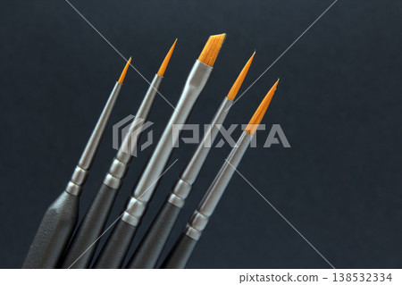 Brushes are lined up on a dark surface showing different sizes and shapes for painting or artwork Brushes are lined up on a dark surface showing different sizes and shapes for painting or artwork 138532334