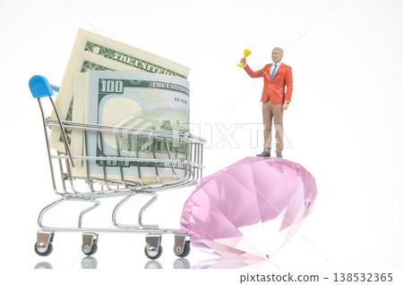Miniature figure stands on a pink gem beside money in a shopping cart in a studio setting Miniature figure stands on a pink gem beside money in a shopping cart in a studio setting 138532365