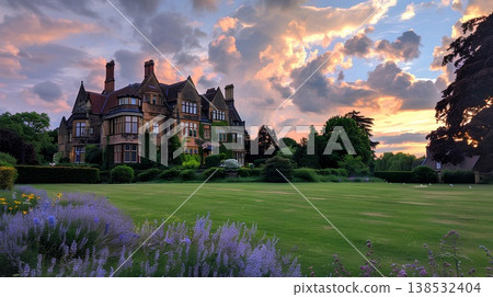 wide view at twilight of a beautiful english mansion with a large lawn and purple flowers, with clouds in the sky wide view at twilight of a beautiful english mansion with a large lawn and purple flowers, with clouds in the sky 138532404