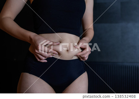 A young woman pinches the excess fat on her slightly overweight belly. 138532408