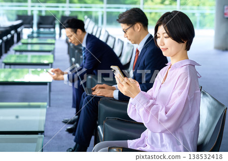 在機場候機室或飯店大廳使用智慧型手機或筆記型電腦的商務人士。 在機場候機室或飯店大廳使用智慧型手機或筆記型電腦的商務人士。 138532418