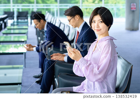 一位女士在辦公室休息室裡面微笑地看著智慧型手機,一位商務人士則在電腦前工作。 一位女士在辦公室休息室裡面微笑地看著智慧型手機,一位商務人士則在電腦前工作。 138532419