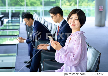 一位女商人面帶微笑，在休息室使用智慧型手機工作。 138532420