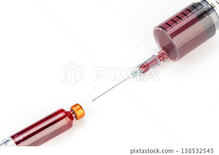 Close-Up Medical Syringe With Sharp Hypodermic Needle Aimed At Small Red Liquid Medication Vial With Gold Cap On Clean White Background Studio Shot 138532545