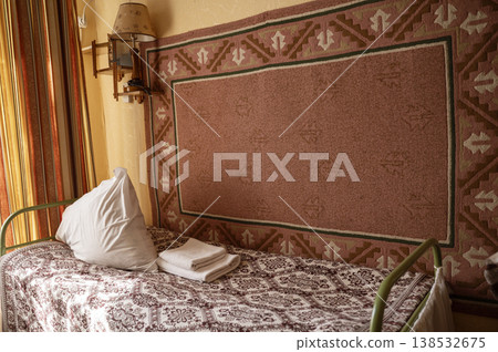 Old vintage bed with a metal headboard and a decorative wall carpet.  138532675