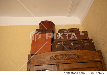 Vintage suitcases and a round hat box stacked on top of a wooden wardrobe 138532677