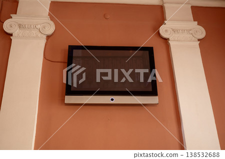 Modern television mounted on a wall between classic columns. Fusion of new technology Modern television mounted on a wall between classic columns. Fusion of new technology 138532688